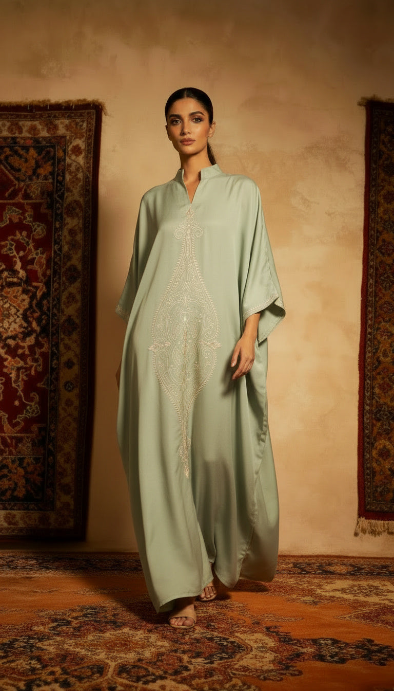 Woman wearing a light green dress with intricate patterns in a room with patterned rugs.