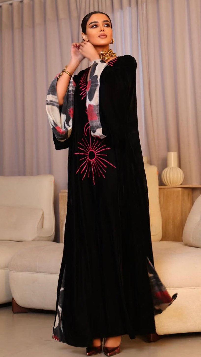 Woman wearing a black abaya with red and white patterns in a living room setting.