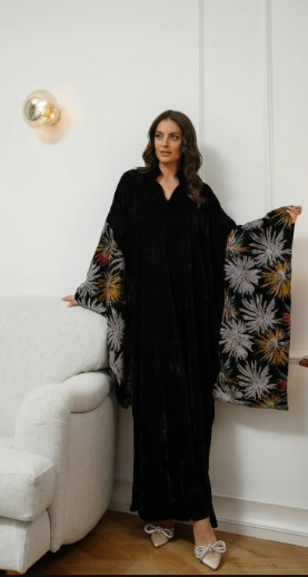 Woman in a black floral dress standing next to a white sofa and a decorative pillow with a floral pattern.