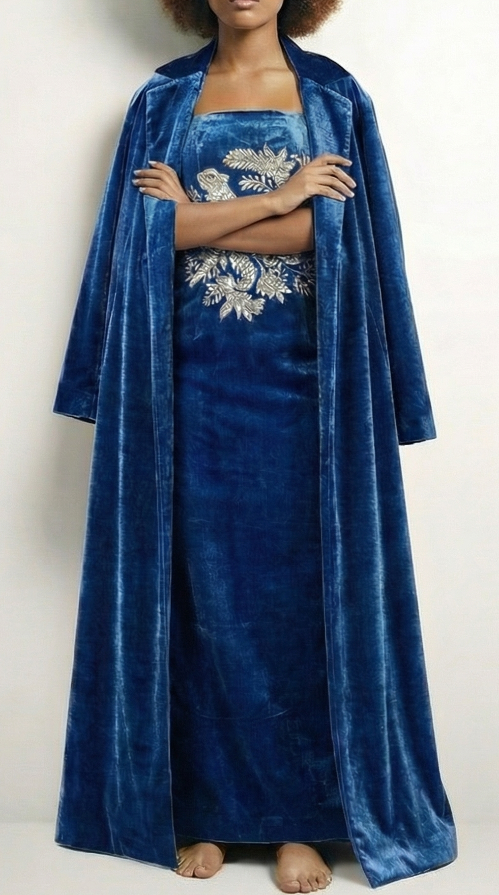 Person wearing a blue velvet dress with floral embroidery on a white background