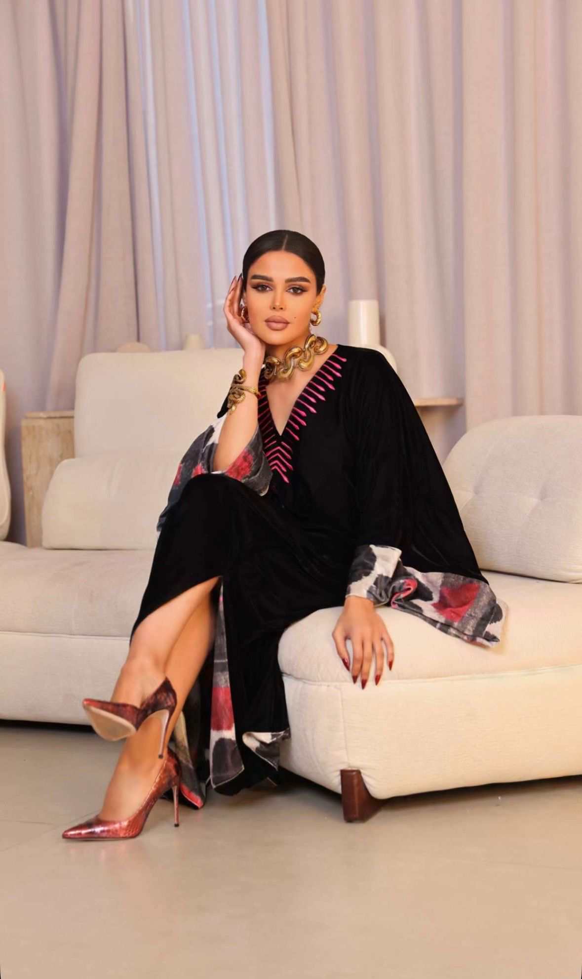 Woman in a black outfit with a colorful scarf sitting on a couch.