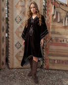 Woman in a black dress with white patterns standing in front of patterned rugs.