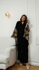 Woman wearing a black outfit with floral sleeves in a room with a white sofa and wall.