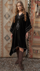 Woman wearing a black dress with white patterns in front of a patterned wall.