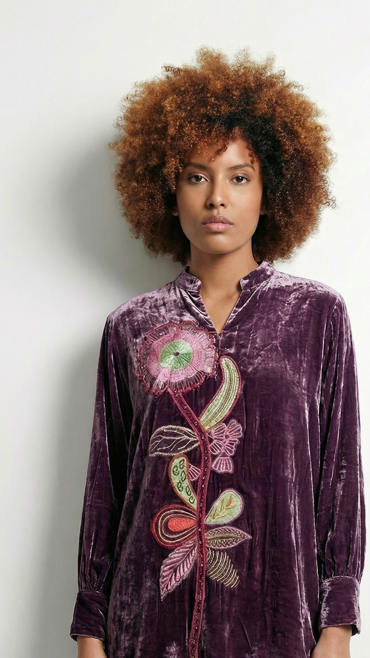 Woman wearing a purple velvet shirt with floral embroidery on a plain background