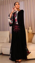 Woman wearing a black abaya with red and white patterns in a living room setting.