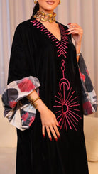 Woman wearing a black dress with pink embroidery in a living room setting