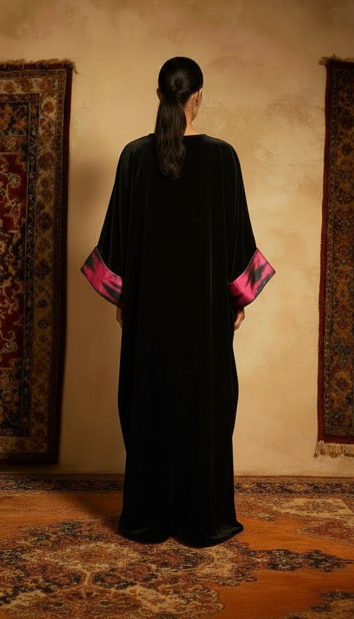 Person wearing a black dress with pink accents standing in front of two patterned rugs on a beige wall.