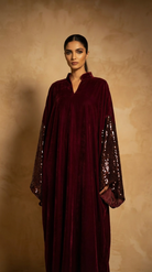 Woman wearing a burgundy velvet dress with sequin sleeves against a beige background