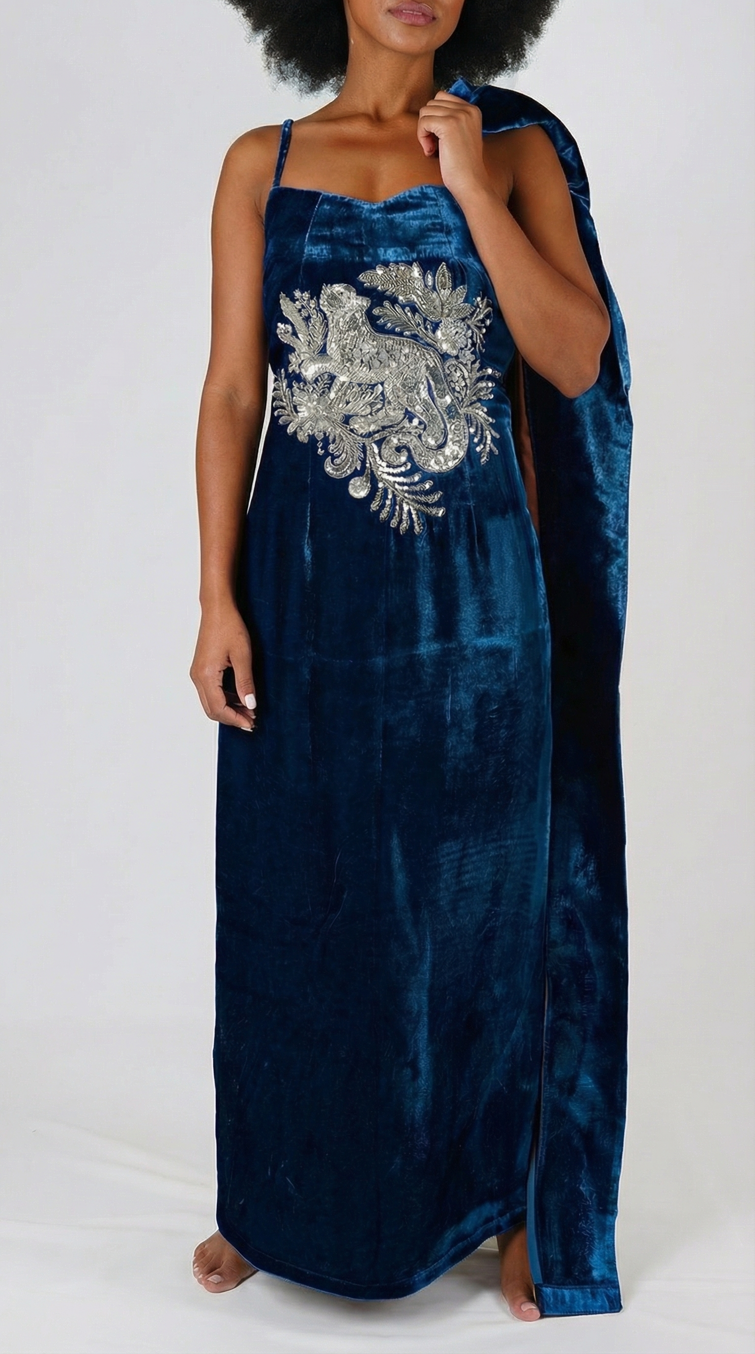Woman wearing a blue velvet dress with silver embroidery on a white background