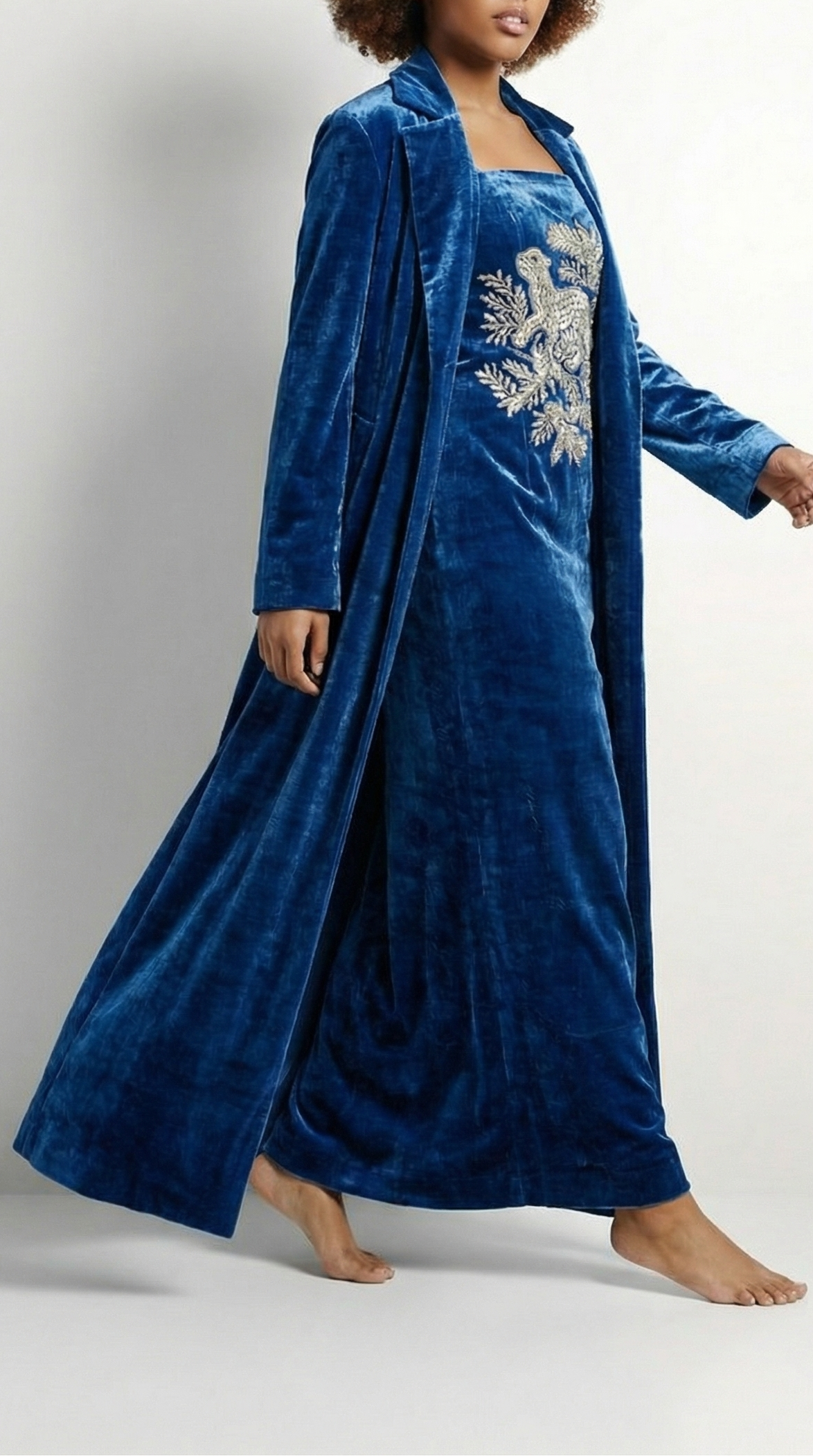 Woman wearing a blue velvet robe with floral embroidery on a white background